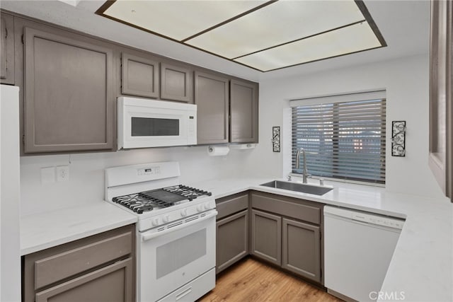 kitchen featuring light wood finished floors, white appliances, light countertops, and a sink