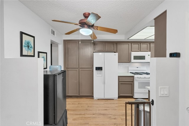 kitchen with white appliances, light wood-style flooring, visible vents, and a textured ceiling