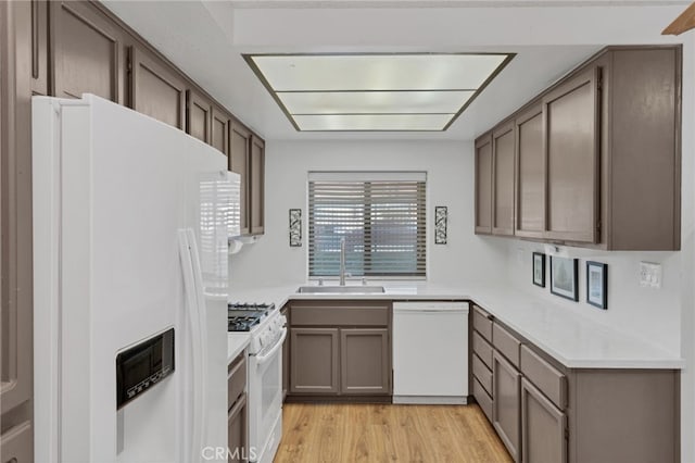 kitchen featuring light wood-style flooring, white appliances, light countertops, and a sink