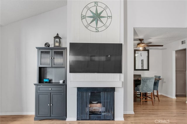 living area with a ceiling fan, a textured ceiling, wood finished floors, a fireplace, and baseboards