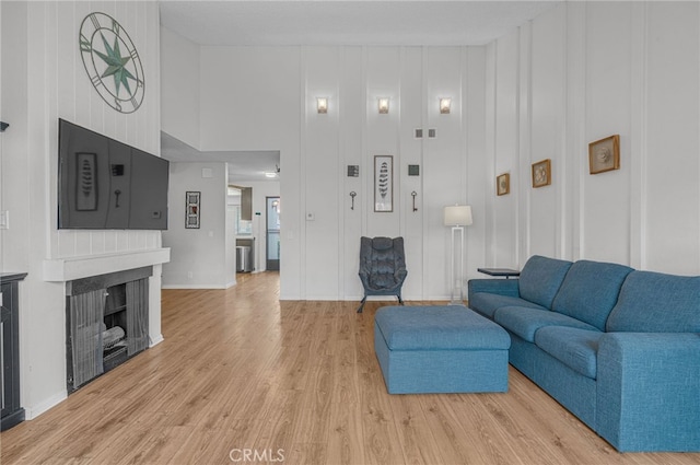 living area featuring visible vents, baseboards, a fireplace, a towering ceiling, and light wood-type flooring