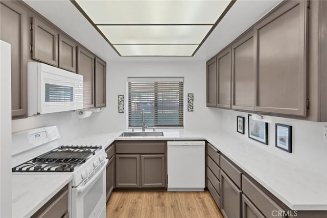 kitchen with light wood-style flooring, white appliances, light countertops, and a sink