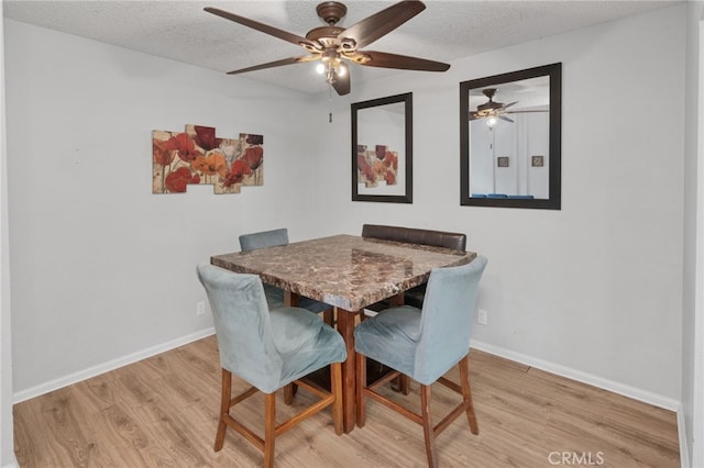 dining space featuring baseboards, a textured ceiling, and light wood-style flooring