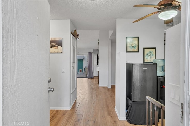 corridor featuring baseboards, light wood-type flooring, and a textured ceiling