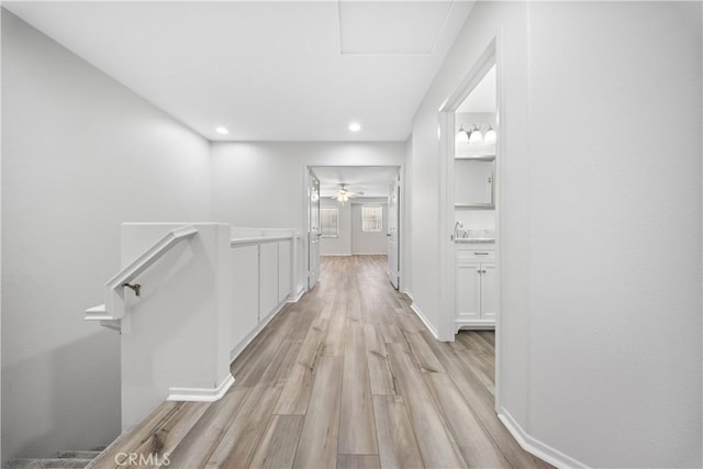 hallway with light wood finished floors, baseboards, an upstairs landing, recessed lighting, and a sink