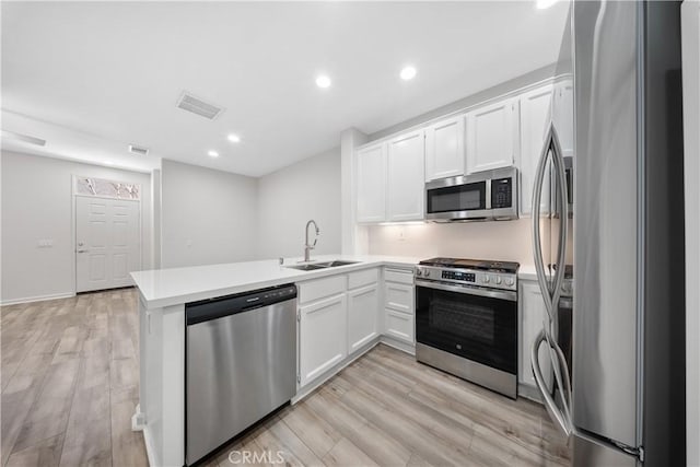 kitchen with visible vents, a sink, appliances with stainless steel finishes, a peninsula, and light wood finished floors