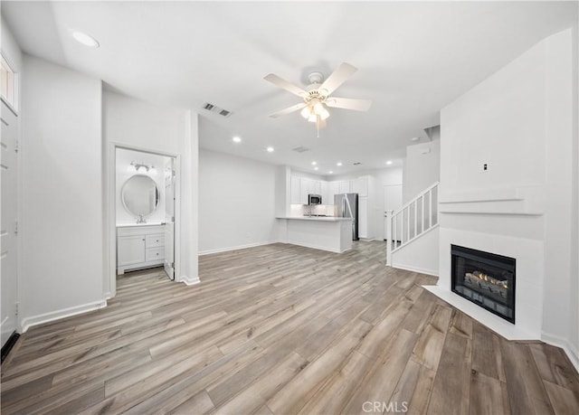 unfurnished living room with a ceiling fan, visible vents, a fireplace with flush hearth, recessed lighting, and light wood-style floors