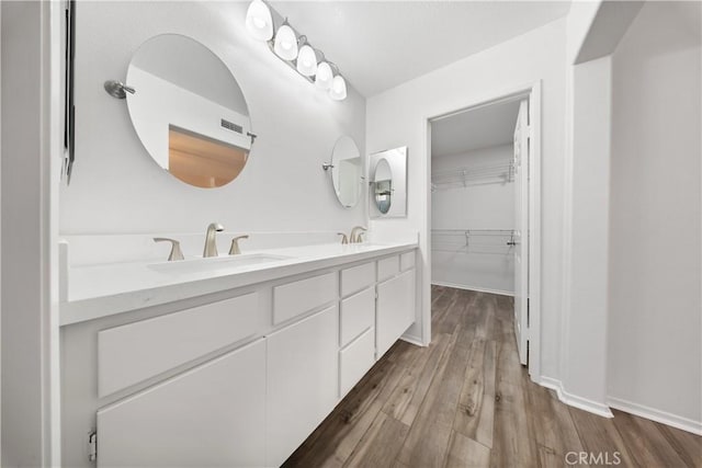 bathroom with a sink, a walk in closet, wood finished floors, and double vanity