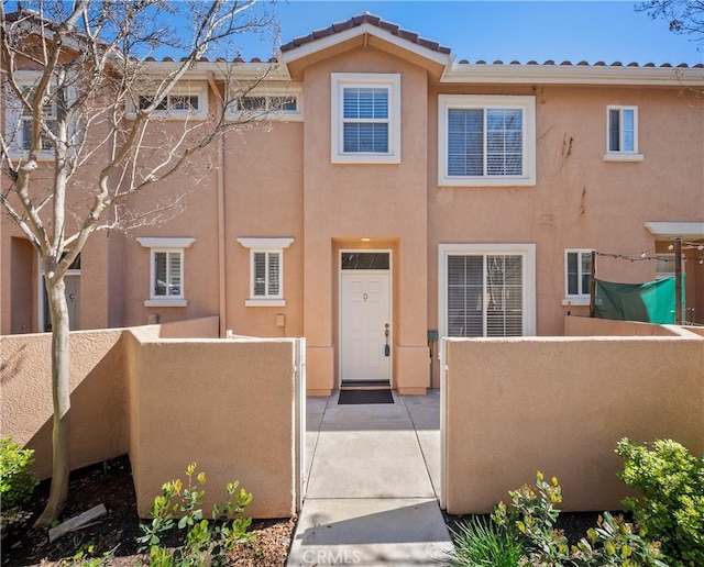 townhome / multi-family property with a tiled roof, fence private yard, and stucco siding