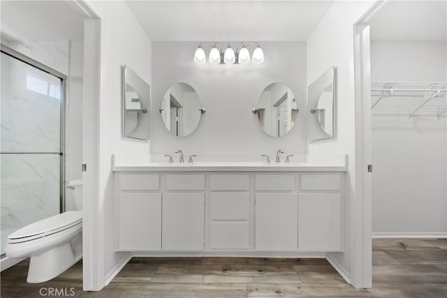 full bath featuring a marble finish shower, double vanity, toilet, and wood finished floors