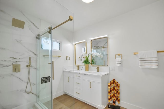 full bath with a sink, a marble finish shower, wood finished floors, and double vanity