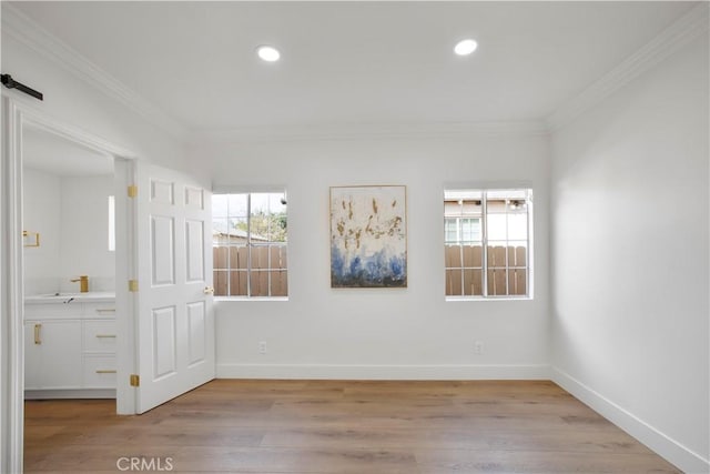 spare room featuring baseboards, a healthy amount of sunlight, light wood-type flooring, and ornamental molding