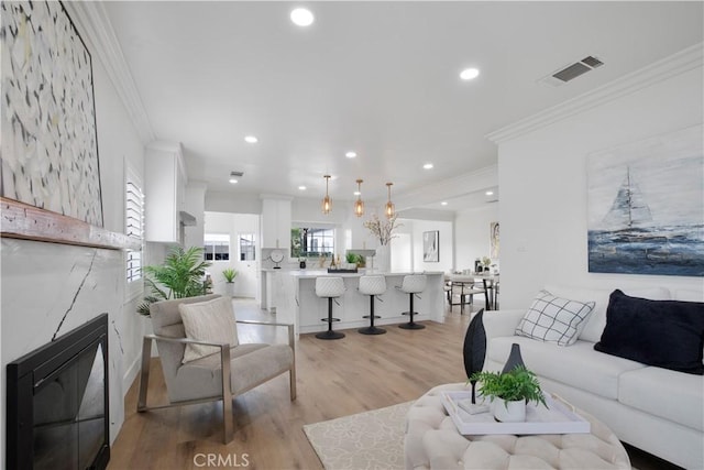 living area with visible vents, light wood finished floors, a premium fireplace, recessed lighting, and ornamental molding