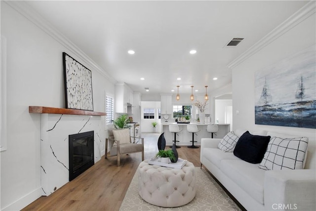 living room with a high end fireplace, visible vents, ornamental molding, light wood-style flooring, and recessed lighting