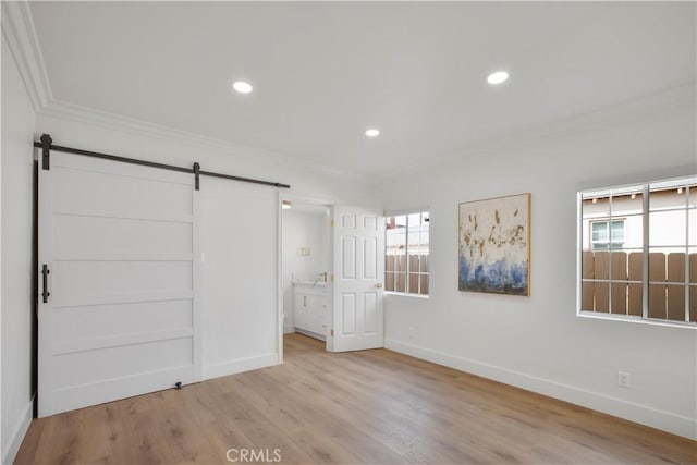 unfurnished bedroom with a barn door, multiple windows, wood finished floors, and crown molding