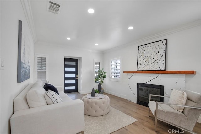 living room with wood finished floors, visible vents, a fireplace, recessed lighting, and ornamental molding