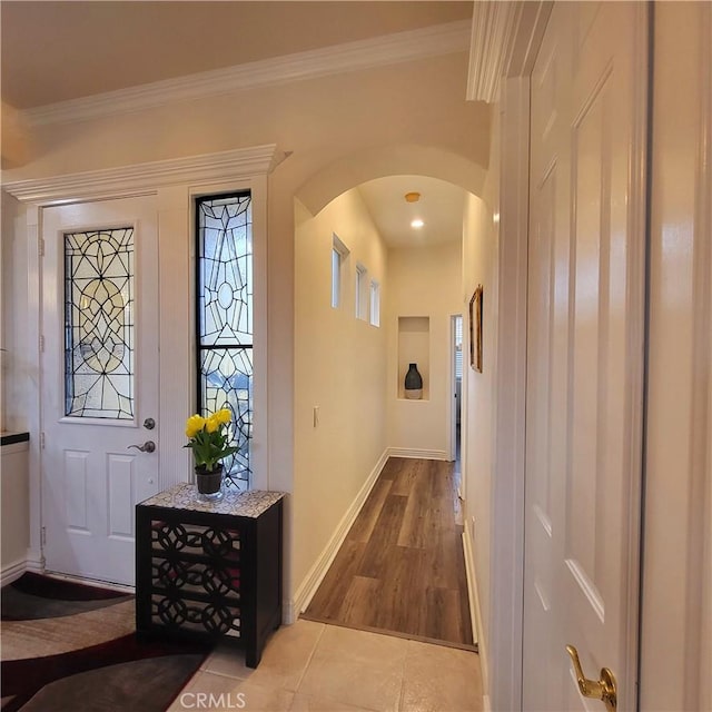 foyer entrance featuring arched walkways, wood finished floors, baseboards, and ornamental molding