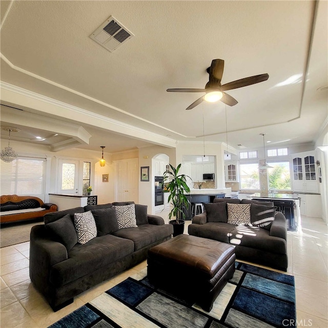 living area with visible vents, arched walkways, ornamental molding, ceiling fan, and light tile patterned flooring