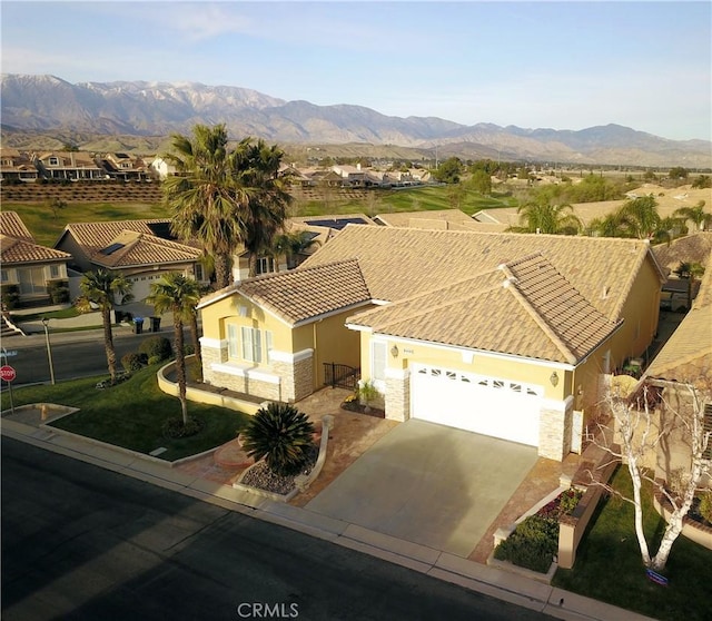 view of front of home with stucco siding, driveway, stone siding, a mountain view, and an attached garage