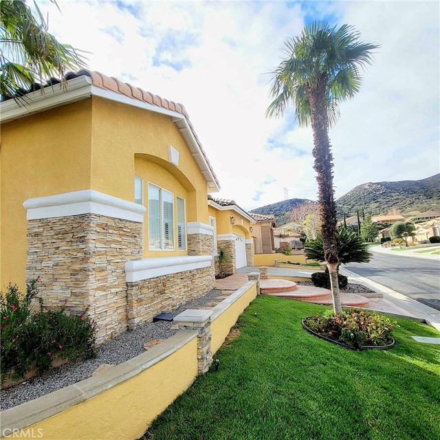 view of home's exterior featuring stucco siding, a mountain view, stone siding, a yard, and a tiled roof