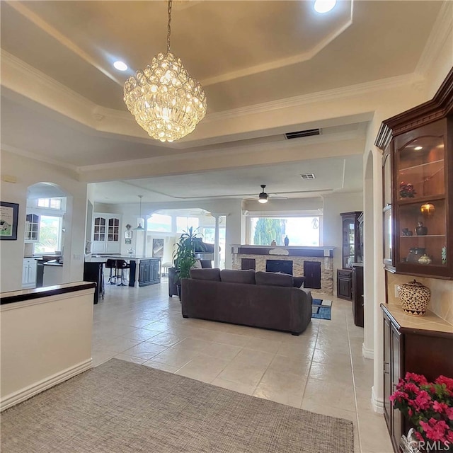 living room with crown molding, ceiling fan with notable chandelier, a tray ceiling, visible vents, and light tile patterned flooring