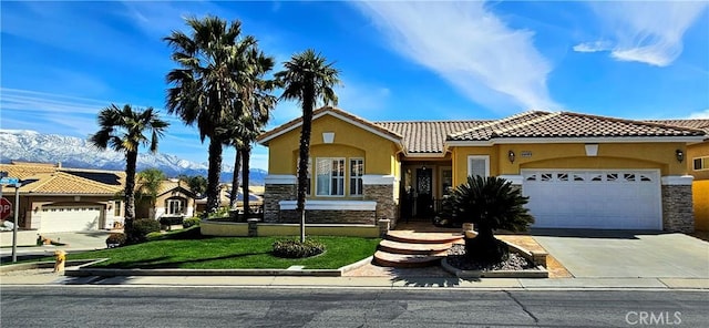 mediterranean / spanish-style house with stucco siding, stone siding, an attached garage, and a tile roof