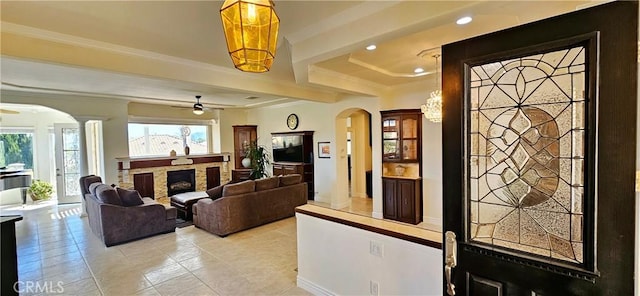 living area with crown molding, light tile patterned floors, ceiling fan, arched walkways, and a fireplace