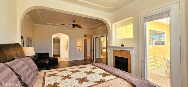 bedroom featuring a fireplace, wood finished floors, arched walkways, and crown molding