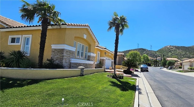 exterior space with stucco siding, a tile roof, stone siding, a front yard, and a mountain view
