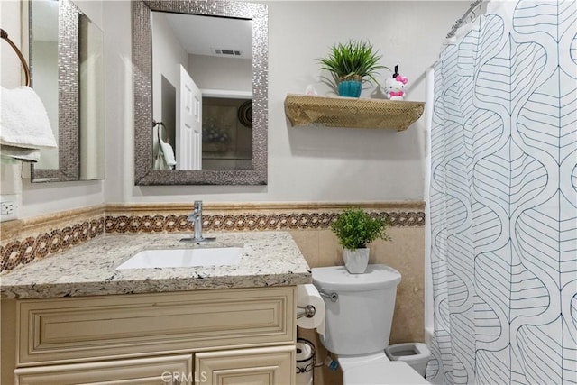 bathroom with a wainscoted wall, toilet, a shower with curtain, tile walls, and vanity