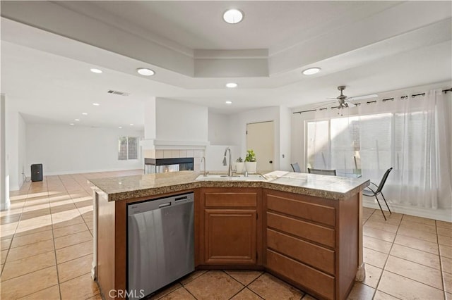 kitchen with a tiled fireplace, open floor plan, a tray ceiling, stainless steel dishwasher, and a sink