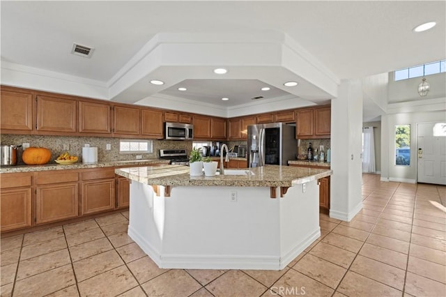 kitchen with light tile patterned floors, stainless steel appliances, brown cabinets, and decorative backsplash