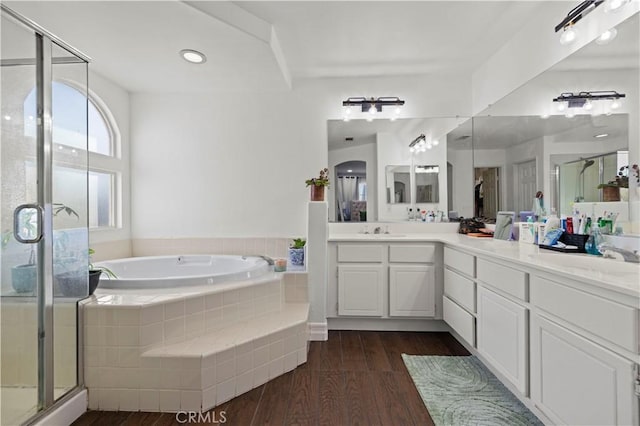 full bath featuring double vanity, wood finished floors, a bath, and a sink