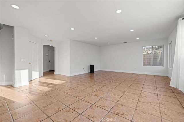 unfurnished living room with light tile patterned flooring, recessed lighting, arched walkways, and baseboards