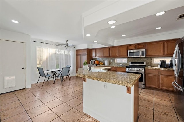 kitchen featuring tasteful backsplash, a sink, brown cabinets, stainless steel appliances, and a kitchen island with sink