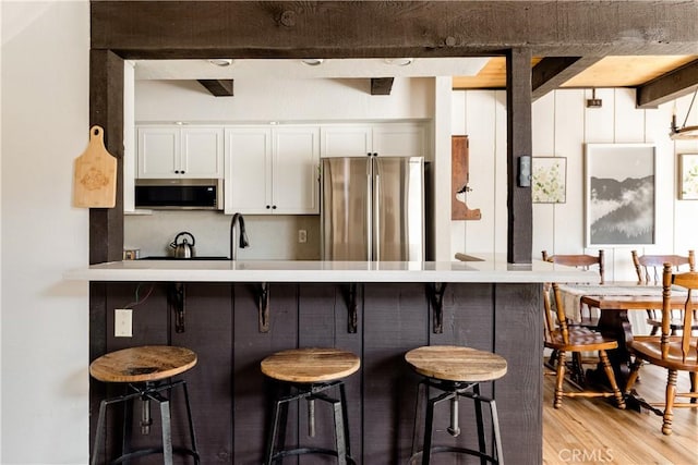 kitchen with stainless steel appliances, light wood finished floors, a kitchen breakfast bar, and white cabinetry