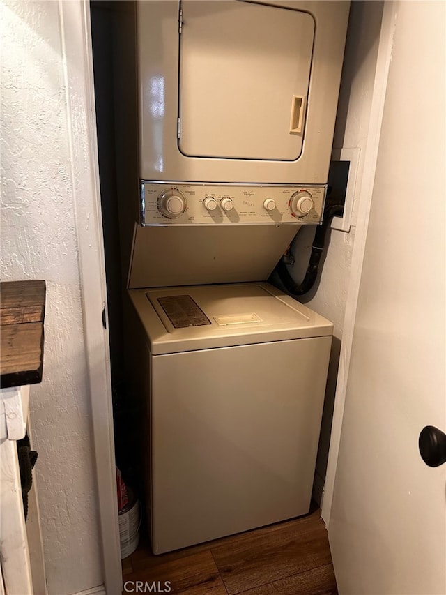 clothes washing area featuring laundry area, stacked washing maching and dryer, wood finished floors, and a textured wall