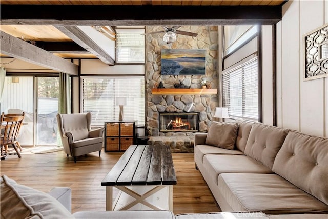 living room with a stone fireplace, wood finished floors, a healthy amount of sunlight, and a ceiling fan