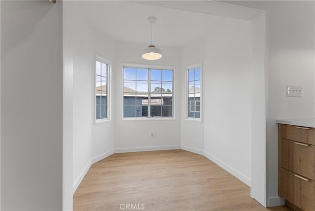 unfurnished dining area with light wood-style flooring and baseboards