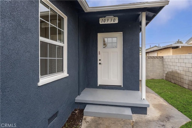 property entrance featuring crawl space, stucco siding, and fence