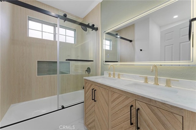 full bathroom with bath / shower combo with glass door, double vanity, and a sink