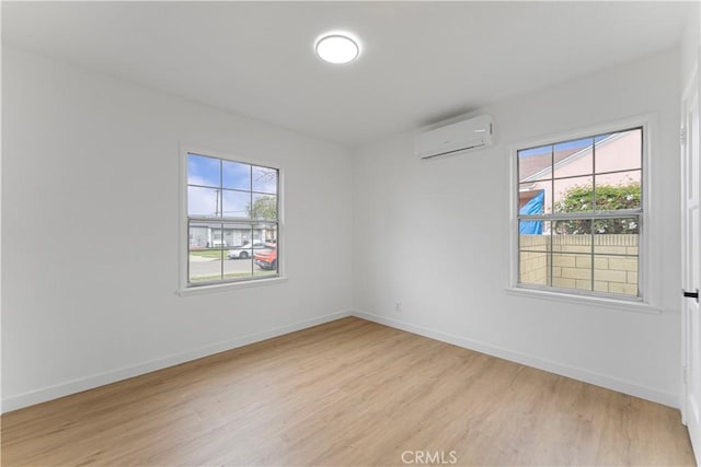 spare room featuring baseboards, plenty of natural light, an AC wall unit, and light wood-style floors