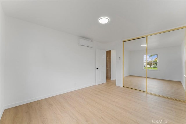 unfurnished bedroom featuring light wood-style flooring, baseboards, and a wall unit AC