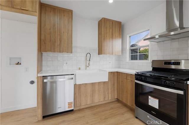 kitchen featuring light countertops, light wood-style flooring, stainless steel appliances, wall chimney exhaust hood, and a sink