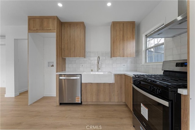 kitchen featuring light wood finished floors, wall chimney range hood, light countertops, appliances with stainless steel finishes, and a sink