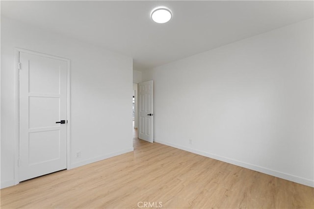 spare room with baseboards and light wood-style floors