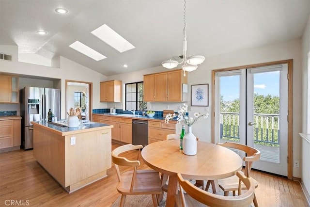kitchen featuring light brown cabinets, a kitchen island, vaulted ceiling with skylight, appliances with stainless steel finishes, and light wood-style floors