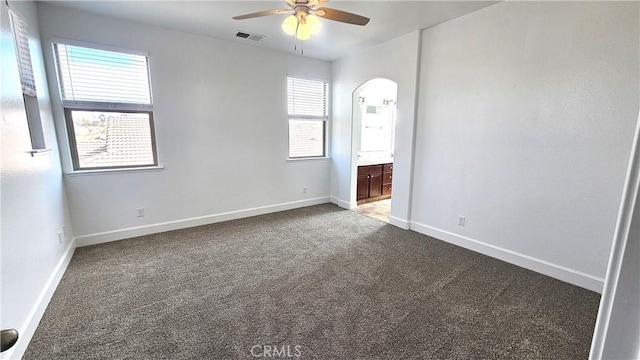 spare room featuring visible vents, a ceiling fan, carpet floors, arched walkways, and baseboards