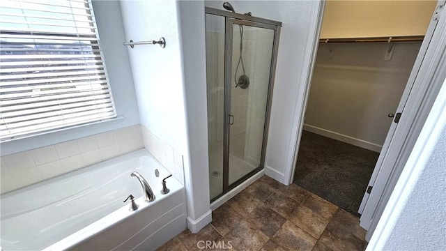 full bath with a stall shower, baseboards, a walk in closet, and a garden tub