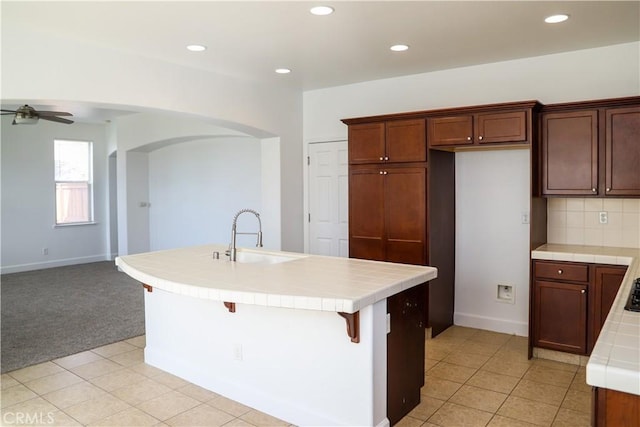 kitchen featuring backsplash, tile countertops, ceiling fan, and a sink